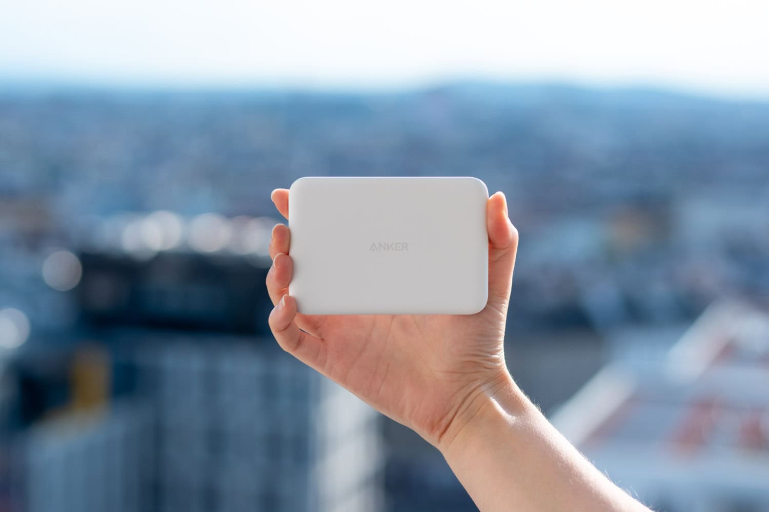 Hand hält tragbare, magnetische Powerbank mit Stadtblick im Hintergrund.